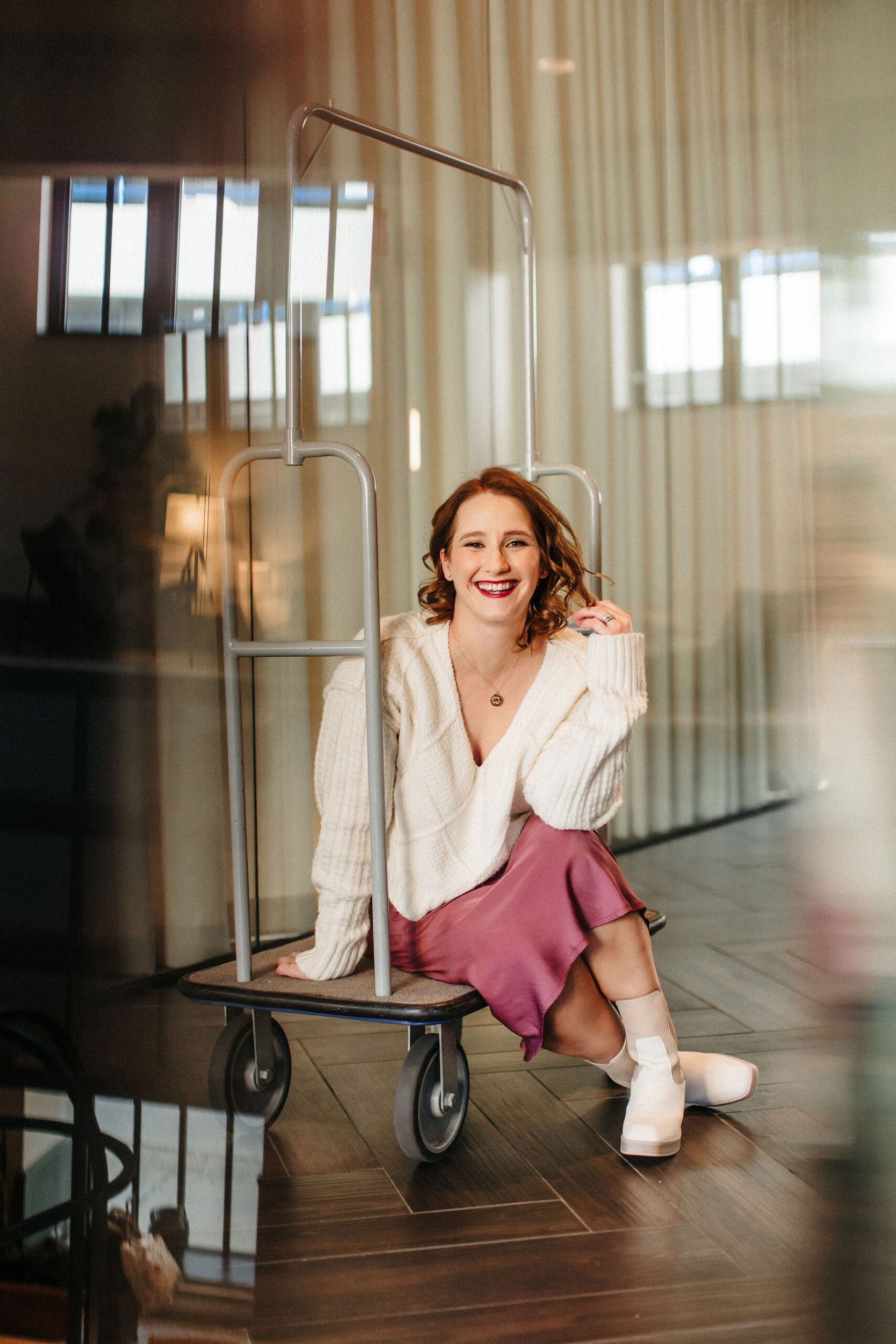 Jenna Leigh sitting on a luggage cart smiling.